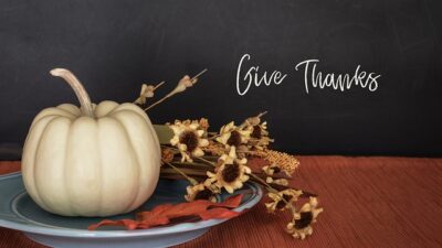 The words Give Thanks with a white pumpkin and fall flower display